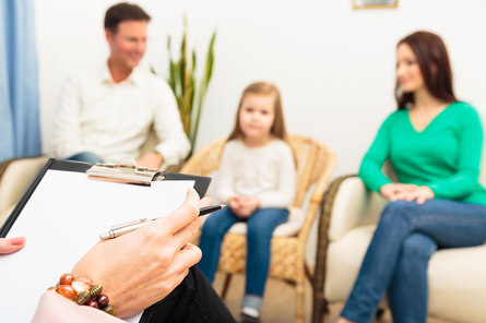 Eine Therapeutin spricht mit einer Familie, zu sehen ist ein Notizblock 