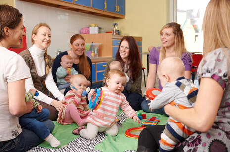 Mütter sitzen mit ihren Kindern zusammen auf dem Boden und unterhalten sich