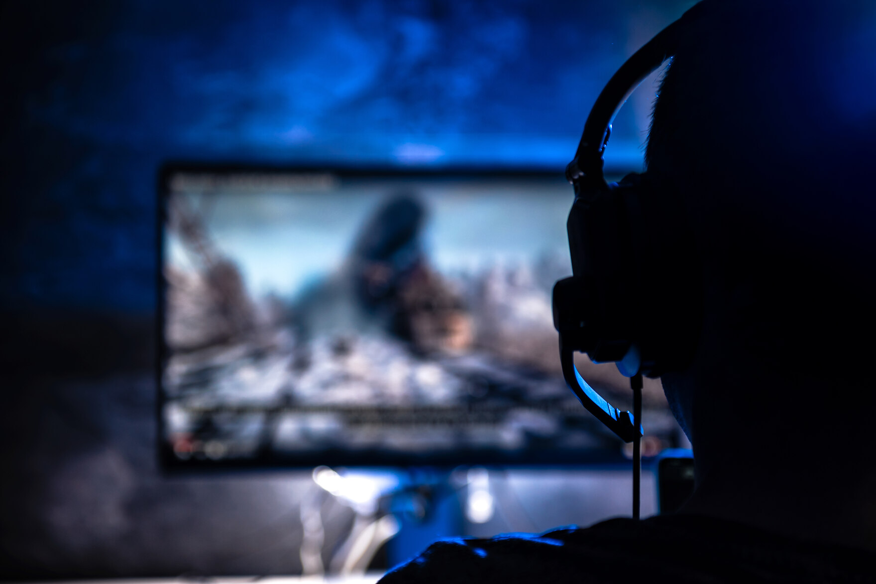 Ein Mensch mit Headset spielt Computer, im Hintergrund ist der Bildschirm zu sehen